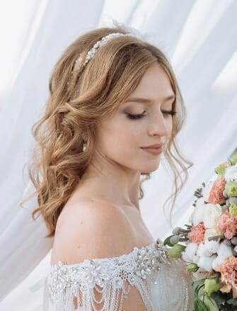 Bride with wavy blonde hair, wearing an off-the-shoulder wedding dress, holding a bouquet of pink and white flowers